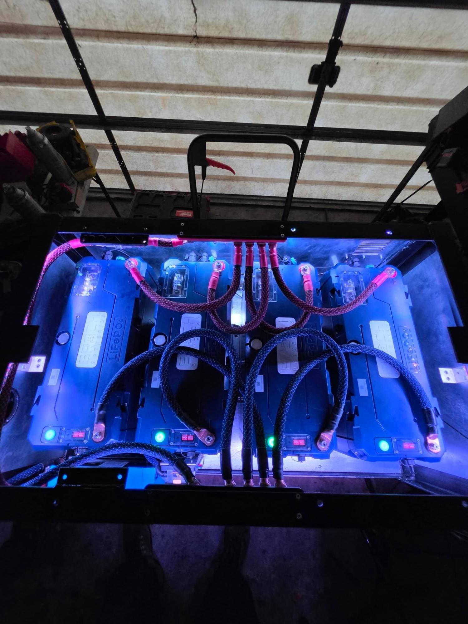 Four Epoch LiFePO4 batteries wired in parallel with braided cables in a blue-lit RV battery compartment