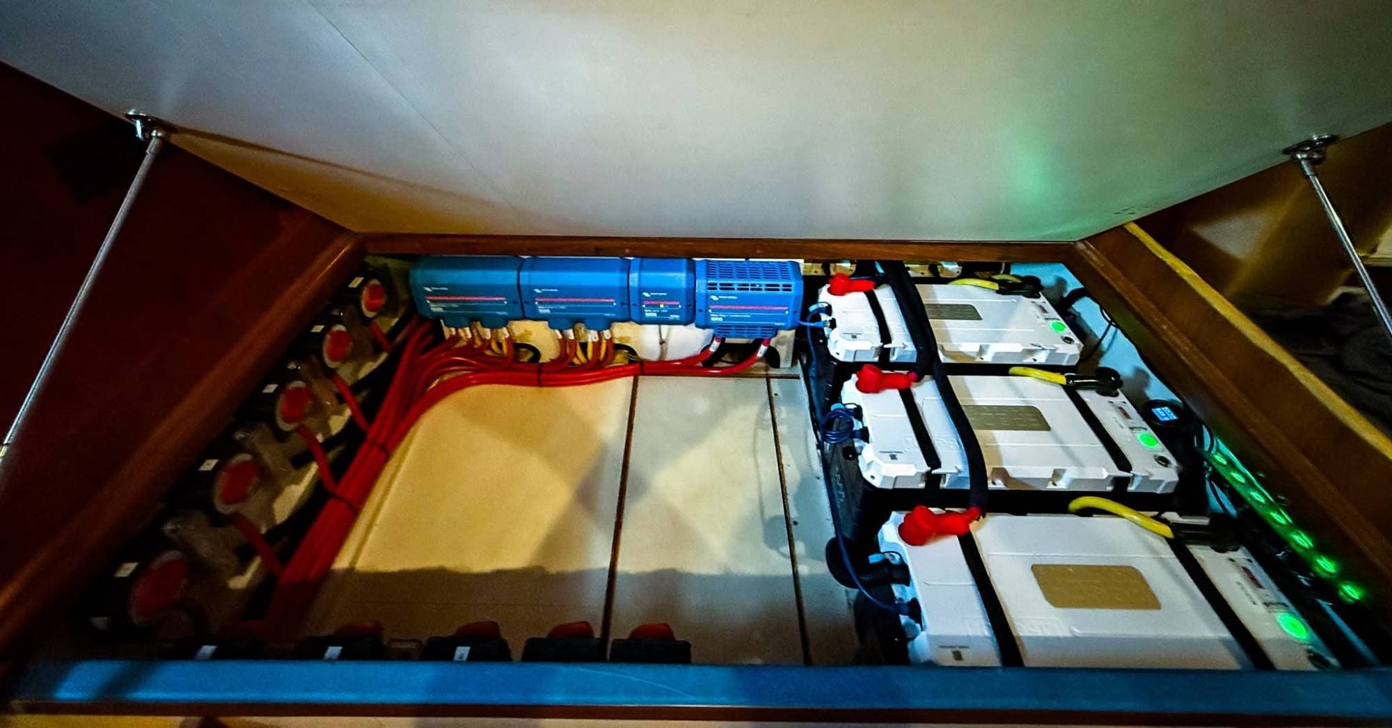 Three Epoch LiFePO4 batteries under a lifted hatch aboard a boat, wired to a row of Victron Lynx modules and battery switches