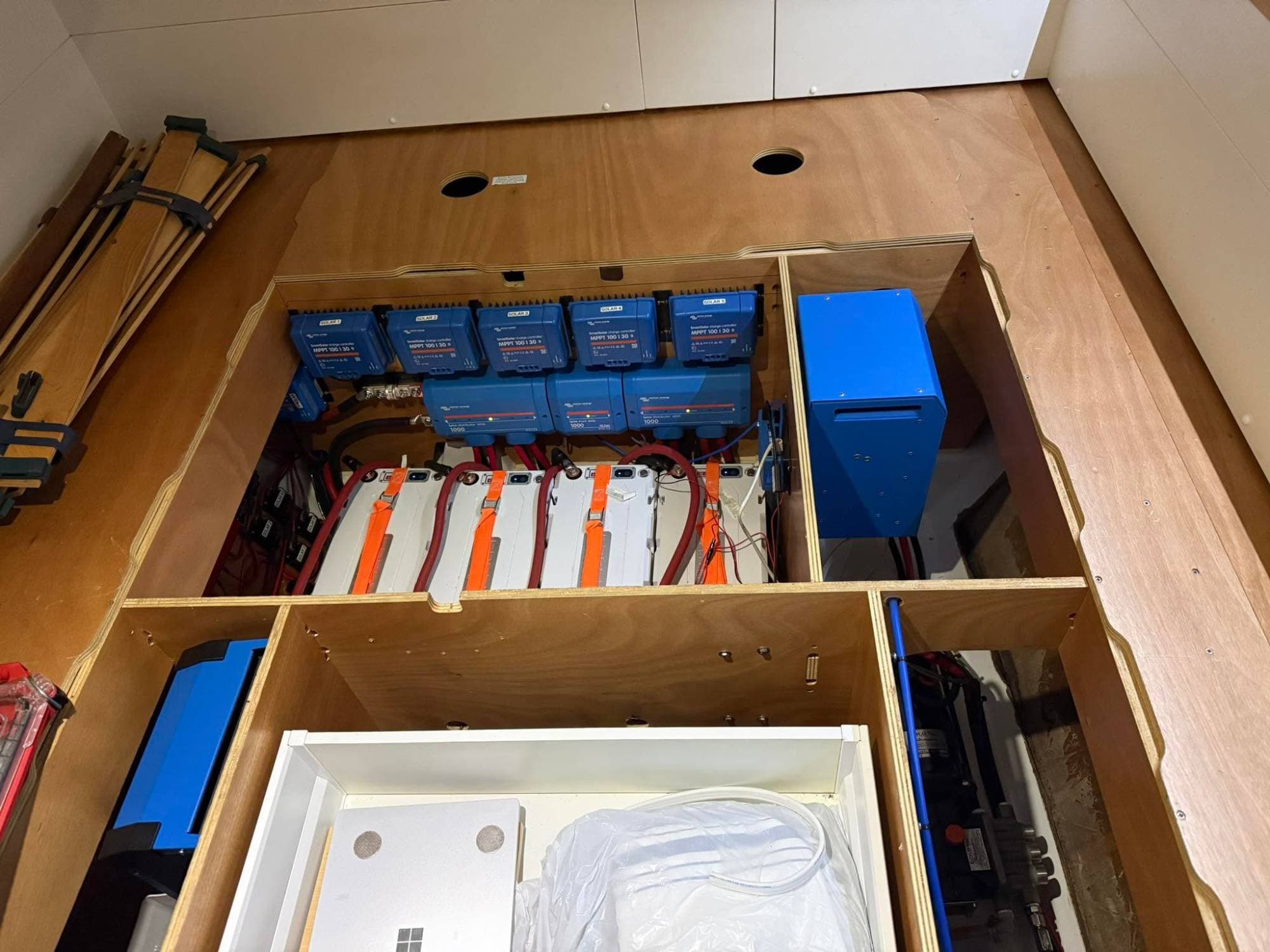 Four Epoch LiFePO4 batteries strapped into a plywood locker aboard a boat, with five Victron SmartSolar charge controllers and Lynx distributors