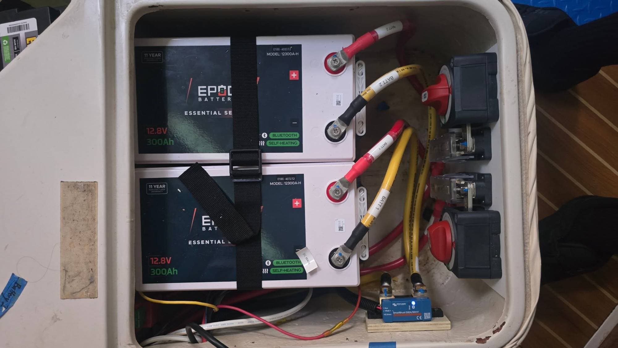 Two Epoch Essential Series 12V 300Ah heated Bluetooth LiFePO4 batteries in a boat's battery locker with two battery switches and a Victron SmartShunt